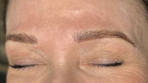 Close-up of a client’s eyebrows after a hairstroke brow treatment, showing soft, natural-looking strokes with eyes closed.
